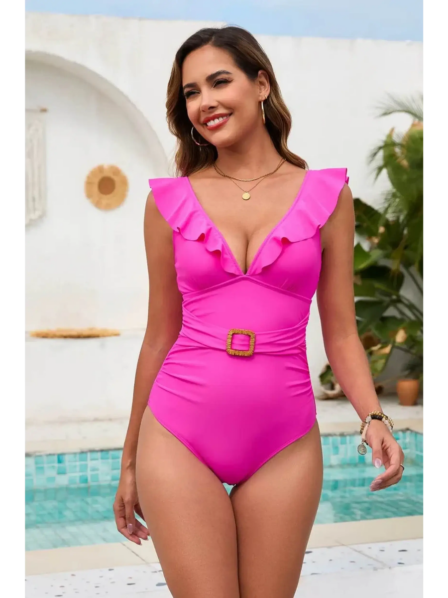 Babe Beachwear flattering one piece swimwear in bright pink with ruffle details and belt by the pool