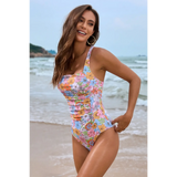 Beach Babes floral one piece swimsuit with multicolor flowers worn by a smiling woman on the beach