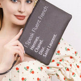 Babe Beachwear black funny quote clutch with French brand names held by woman in floral dress and straw hat