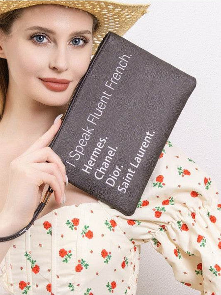 Babe Beachwear black funny quote clutch with French brand names held by woman in floral dress and straw hat