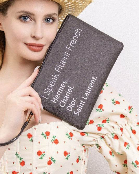 Babe Beachwear black funny quote clutch with French brand names held by woman in floral dress and straw hat