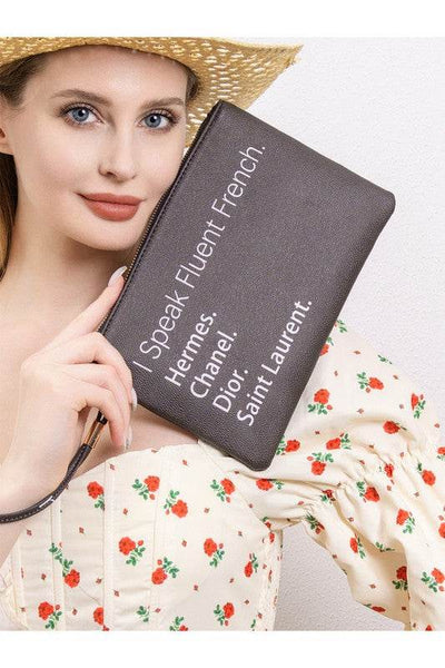 Babe Beachwear black funny quote clutch with French brand names held by woman in floral dress and straw hat