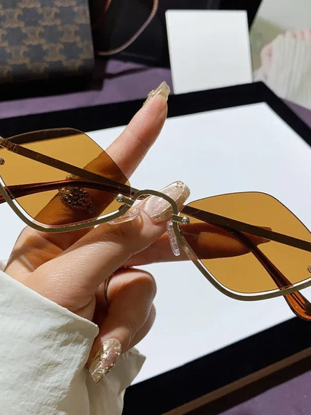 Trendsi glamorous vacation sunglasses with brown tinted lenses and gold metal frame held in hand