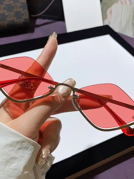 Trendsi glamorous vacation sunglasses with red tinted lenses and gold frame held by hand
