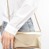 Babe Beachwear gold envelope clutch for women with chain strap worn with white shirt and jeans