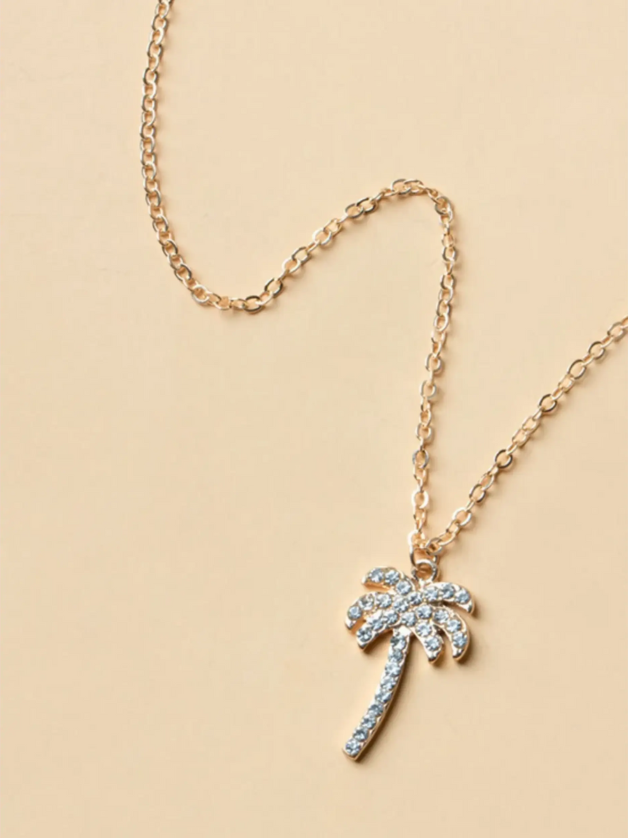 palm tree pendant necklace with sparkling stones and gold chain on beige background