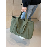 Lightweight Ladies duffle bag in olive green corduroy fabric held by a person wearing jeans and white shoes