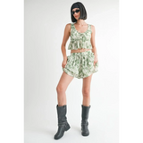 Woman wearing green tropical flutter shorts and matching sleeveless top styled with black boots and sunglasses
