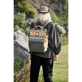 Person wearing a yellow and gray striped Himwari Large waterproof backpack outdoors near rocks and greenery