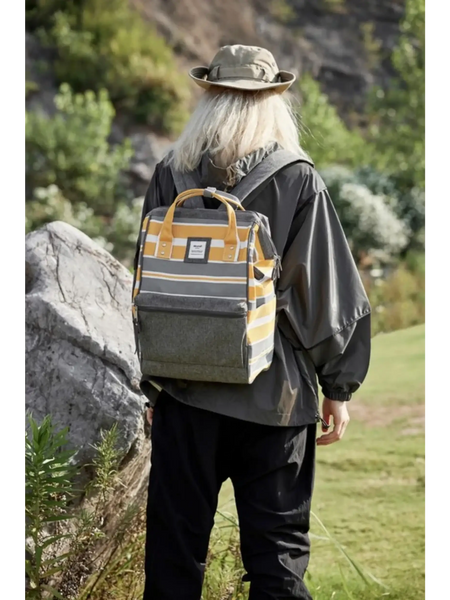 Person wearing a yellow and gray striped Himwari Large waterproof backpack outdoors near rocks and greenery