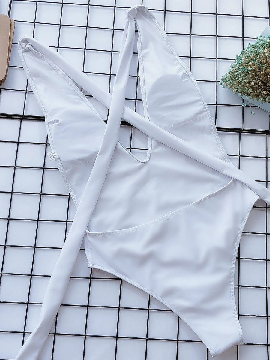 White halter one piece swimsuit from Trendsi laid flat on grid surface with bouquet and purse