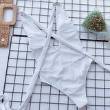 White halter one piece swimsuit from Trendsi laid flat on grid surface with bouquet and purse
