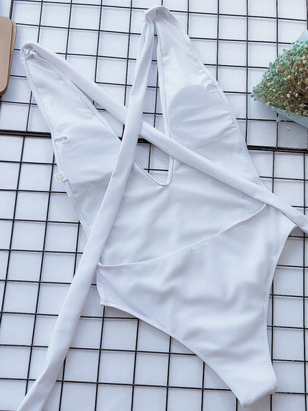 White halter one piece swimsuit from Trendsi laid flat on grid surface with bouquet and purse