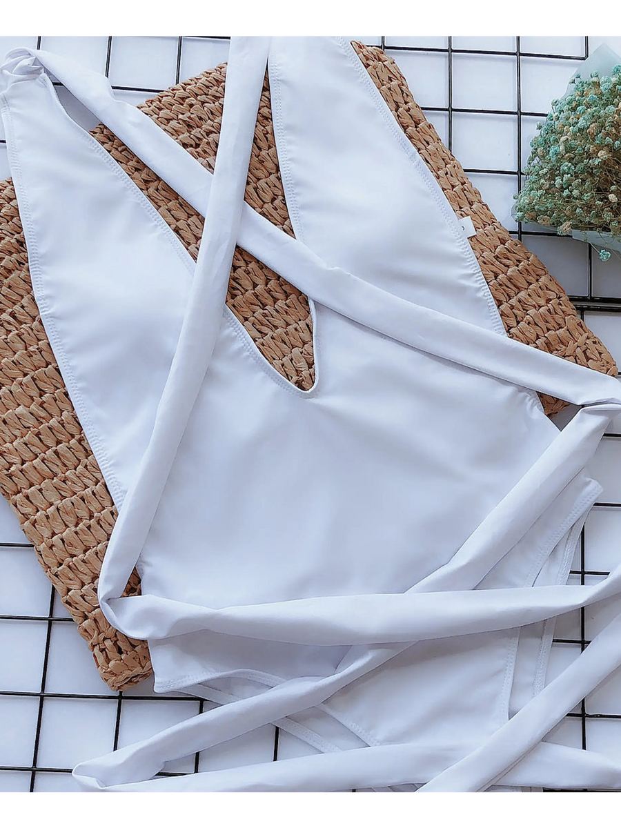 Trendsi white swimsuit laid flat with straps on woven mat and floral decoration background