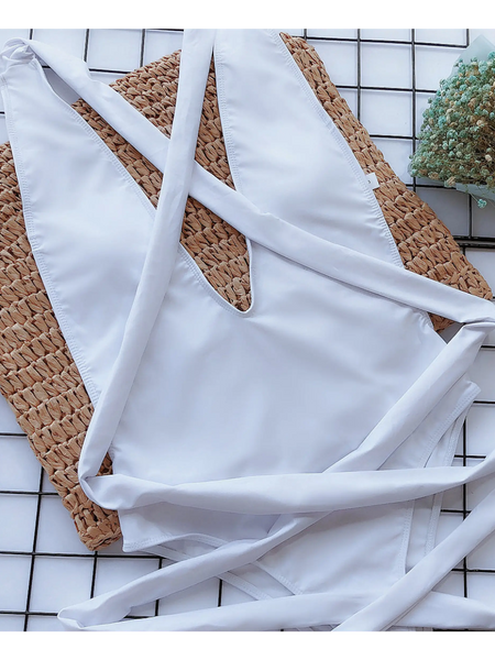 Trendsi white swimsuit laid flat with straps on woven mat and floral decoration background