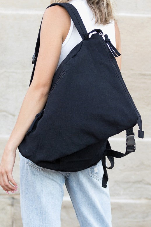 Black Kai Asymetric Canvas Backpack by Babe Beachwaer worn by person with white top and jeans