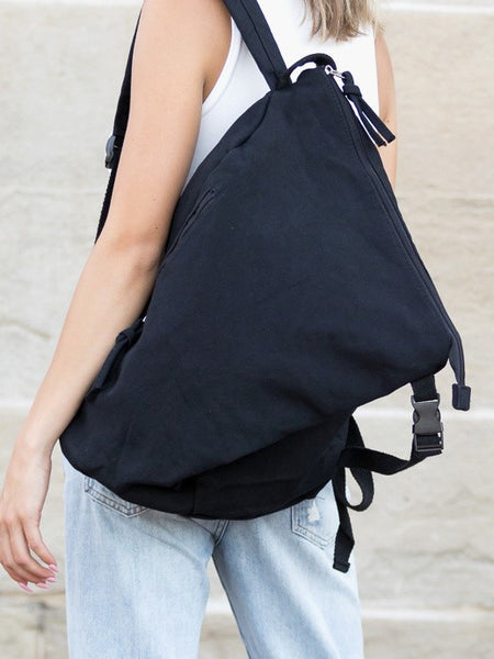 Black Kai Asymetric Canvas Backpack by Babe Beachwaer worn by person with white top and jeans