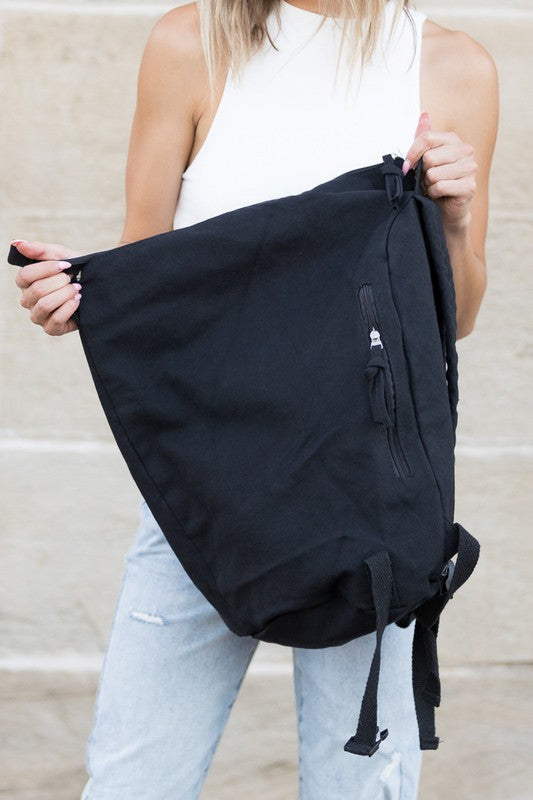 Babe Beachwaer Kai Asymetric Canvas Backpack in black held by woman in white top and jeans