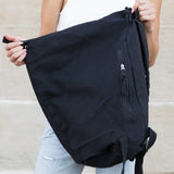 Babe Beachwaer Kai Asymetric Canvas Backpack in black held by woman in white top and jeans