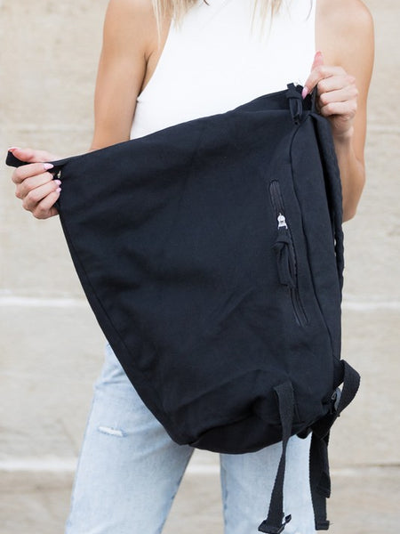 Babe Beachwaer Kai Asymetric Canvas Backpack in black held by woman in white top and jeans
