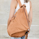 Woman wearing Babe Beachwear Kai Asymetric Canvas Backpack in tan color with side zipper and adjustable straps