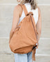 Woman wearing Babe Beachwear Kai Asymetric Canvas Backpack in tan color with side zipper and adjustable straps