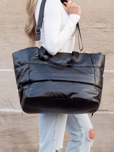 Black large lightweight puffer weekends bag carried by a woman with adjustable shoulder strap