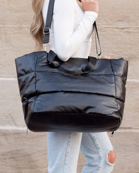 Black large lightweight puffer weekends bag carried by a woman with adjustable shoulder strap