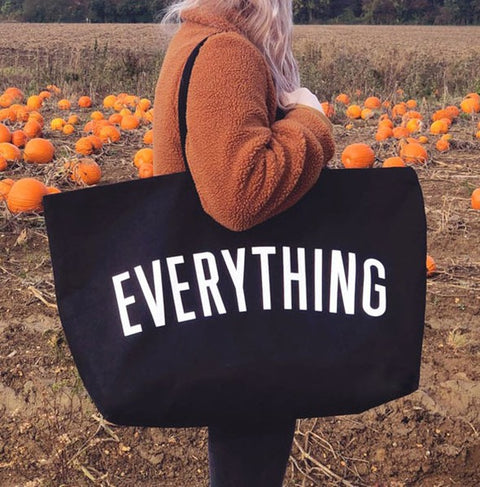 Large oversize everything bag for travel in black with white lettering carried by person in outdoor pumpkin patch