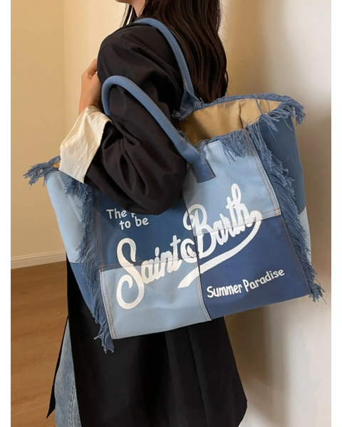 Large resort tote bag with fringe in blue tones featuring Saint Barth text held by a woman
