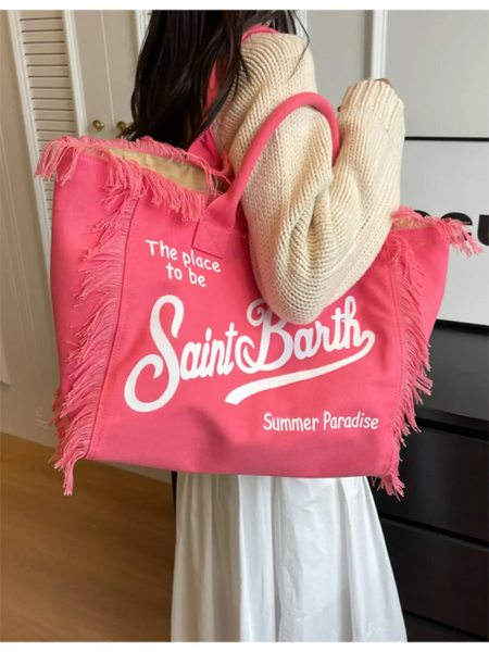Pink large resort tote bag with fringe featuring Saint Barth text worn over shoulder