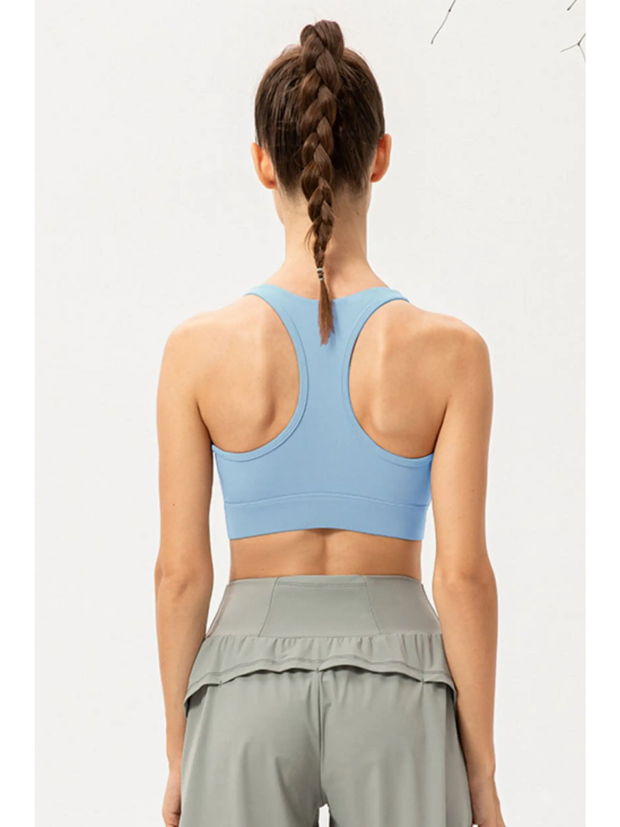Back view of model wearing light blue zip front sports bra by Babe Beachwear with racerback design