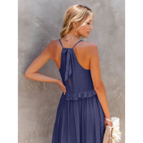 Back view of woman wearing flowy pink ruffle maxi dress with halter neck and bow tie