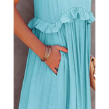 Close-up of a blue maxi dress with ruffle detail and pocket, styled with bracelets and a beige handbag