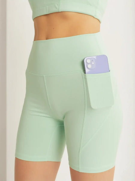 Trendsi mint green high waist active shorts with pocket holding a smartphone