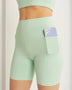Trendsi mint green high waist active shorts with pocket holding a smartphone