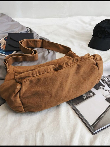 Brown Nova Oversized Canvas Messanger Bag by Babe Beachwaer on white surface with black cap and magazines