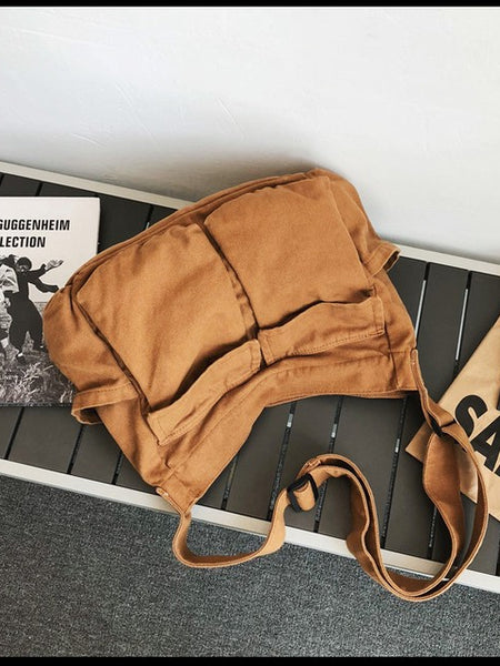 Babe Beachwaer Nova Oversized Canvas Messanger Bag in brown laid on a bench with books