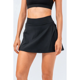 Babe Beachwear black pleated tennis skirt with pockets worn by woman with black crop top