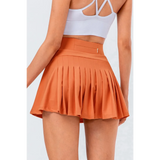 Babe Beachwear pleated tennis skirt with pockets in orange worn by model showing back view