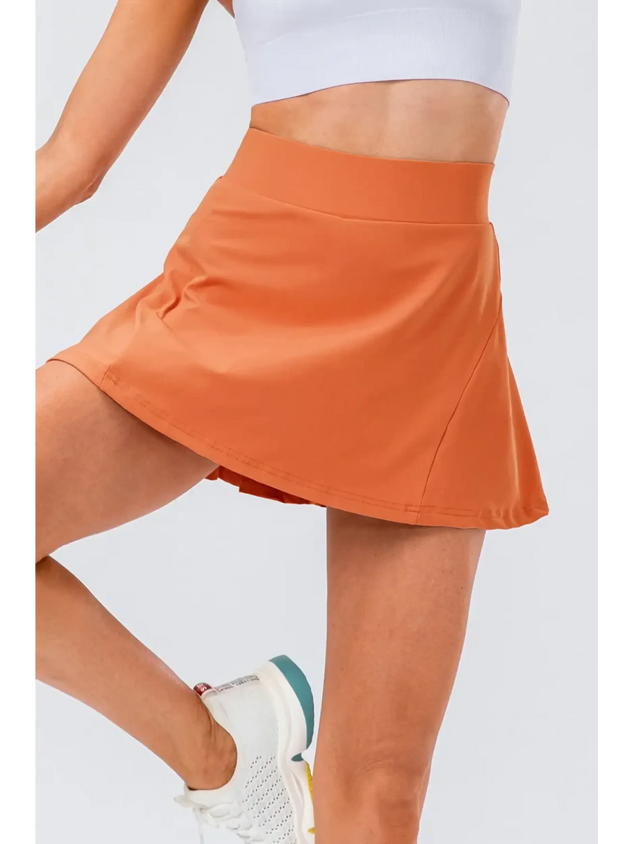 Babe Beachwear orange pleated tennis skirt with pockets worn with white athletic shoes