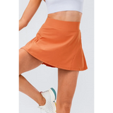 Babe Beachwear orange pleated tennis skirt with pockets worn with white athletic shoes
