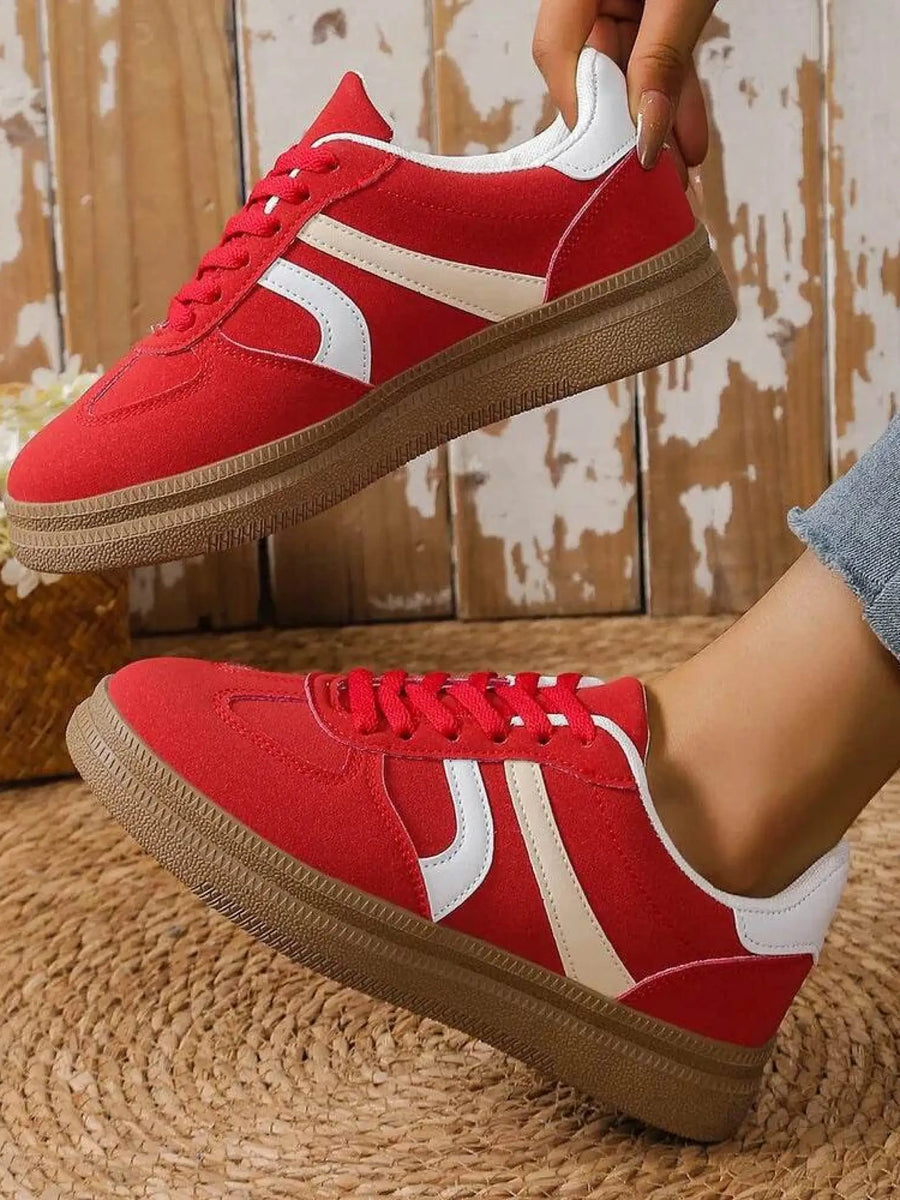 red contrast round toe sneakers with white stripes and brown sole worn with jeans
