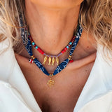 Trendsi resort cruise statement coral necklace featuring red beads and gold fish charms on a blue patterned fabric