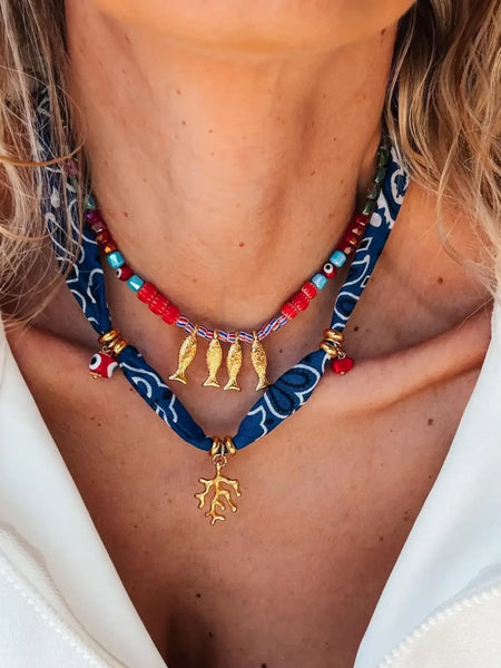 Trendsi resort cruise statement coral necklace featuring red beads and gold fish charms on a blue patterned fabric