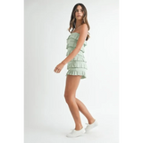 Woman wearing a green ruffled tube romper by Trendsi with white sneakers on a white background