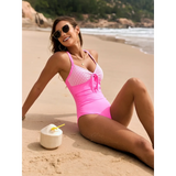 Woman wearing a Beach Babes sexy one-piece bathing suit in pink and white sitting on sandy beach