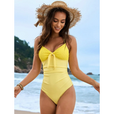 Beach Babes sexy one-piece bathing suit in yellow with a bow detail worn by a woman on the beach