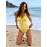 Beach Babes yellow sexy one-piece bathing suit worn by woman kneeling on beach sand by ocean