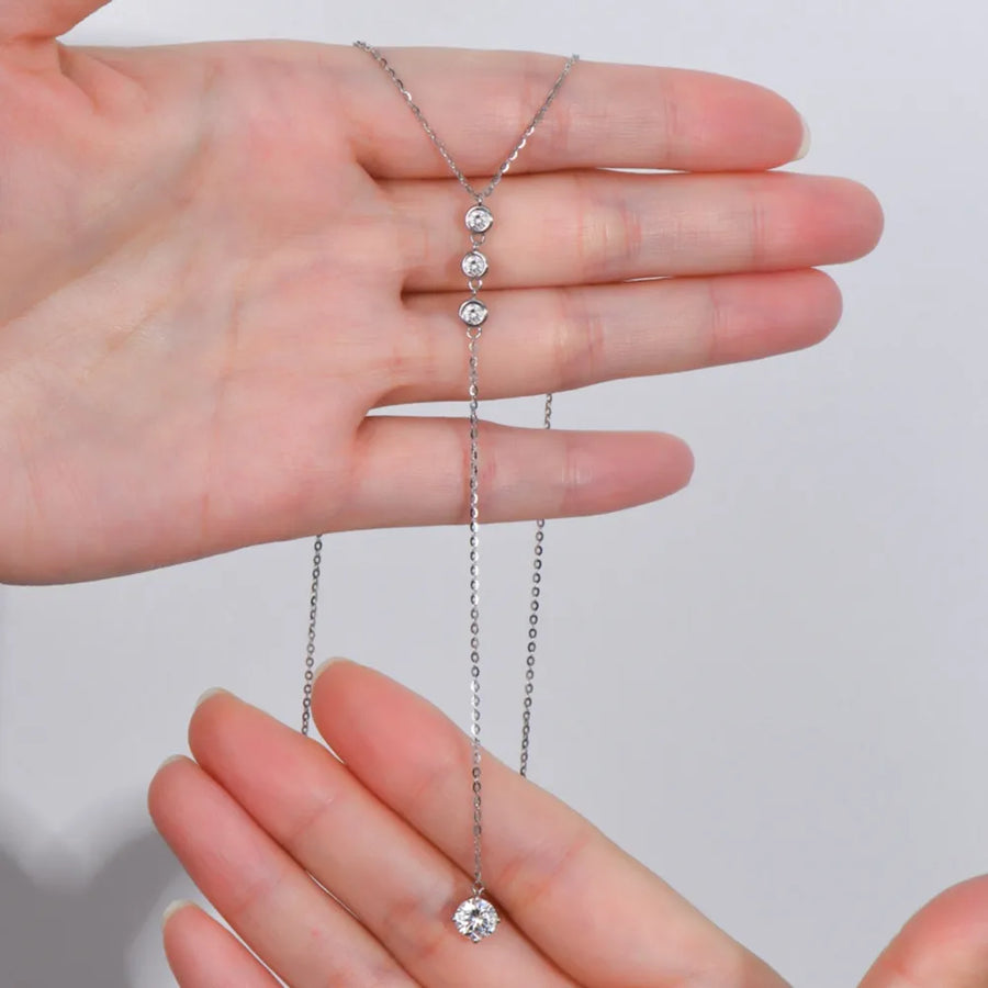 Babe Beachwaer 1.3 carat drop necklace with three small stones and a larger pendant held between hands